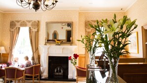A room with a fireplace, a chandelier, and a large mirror. There are chairs and a table with a vase of flowers. - The Ryandale Inn (Dungannon)