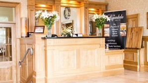 A reception area with a wooden reception desk, two vases with white flowers, a signboard, and a mirror above the desk. - The Ryandale Inn (Dungannon)