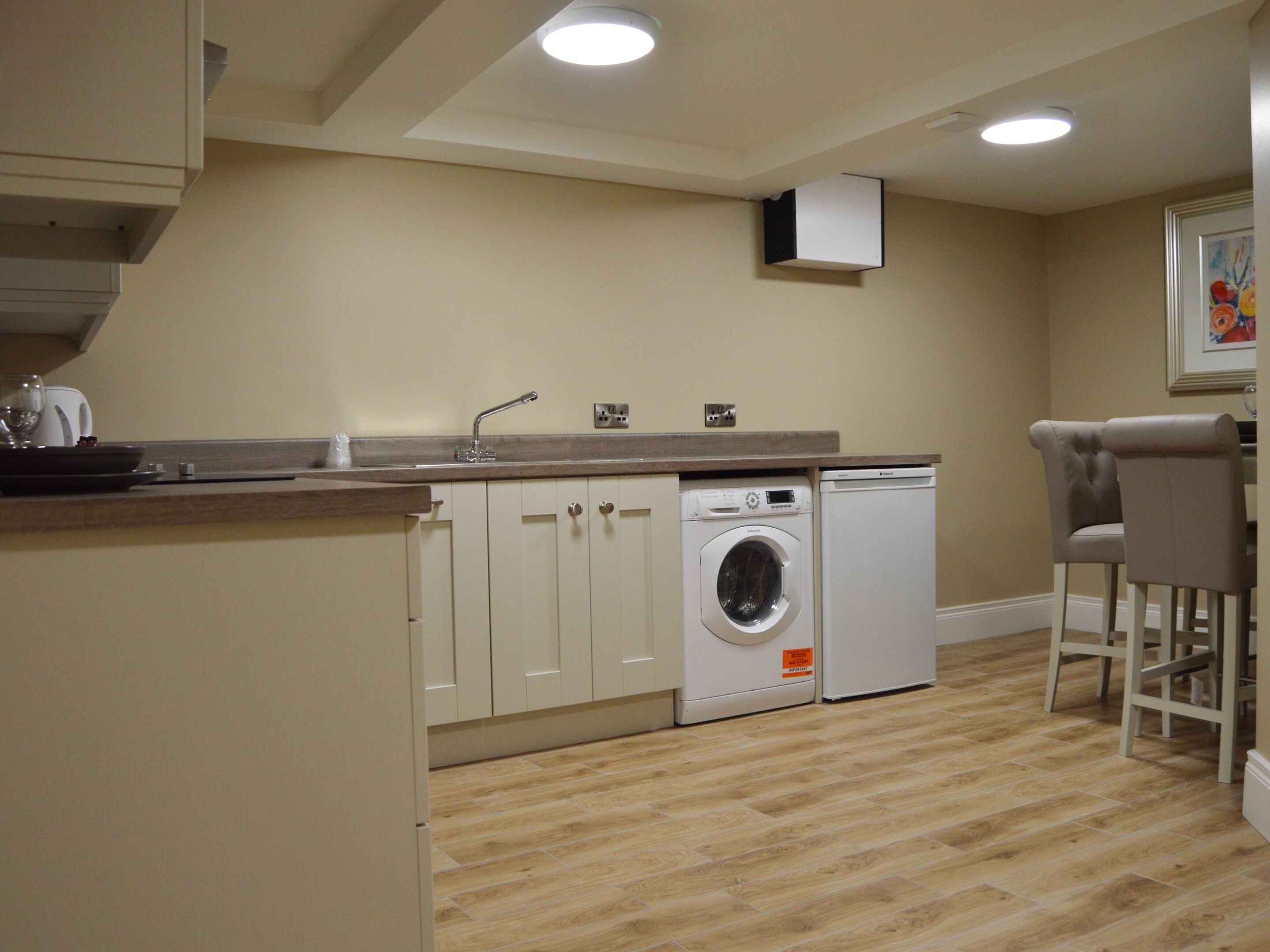 A compact kitchen with a washing machine, a sink, and a dining area with two chairs.