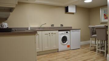 A compact kitchen with a washing machine, a sink, and a dining area with two chairs.