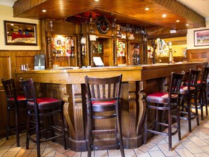 Un espace bar avec des tabourets de bar en bois, une horloge et diverses bouteilles d’alcool.
