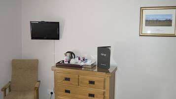 Habitación de hotel con tocador de madera, una silla, televisor montado en la pared y un cuadro enmarcado.