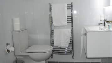 A bathroom with a toilet, a towel rack with two towels, a sink with toiletries, and a trash can.