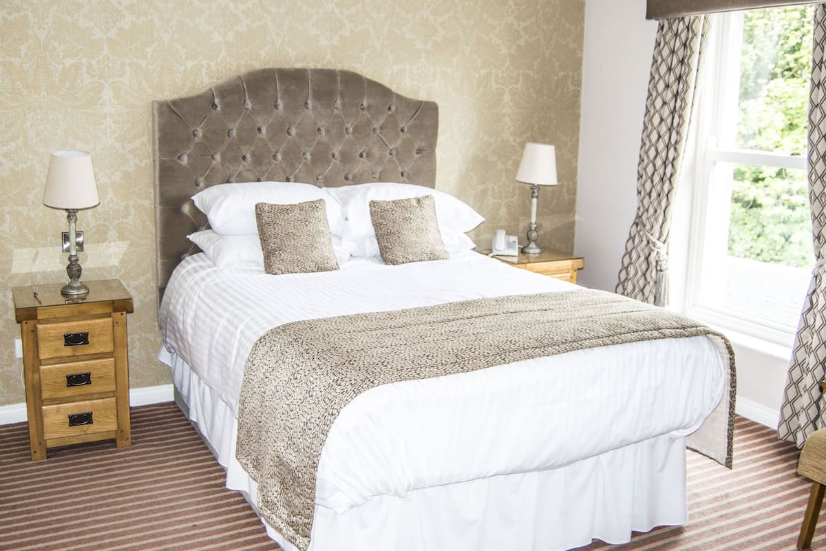 A neatly made bed with a tufted headboard, two bedside tables with lamps, and a window with curtains.