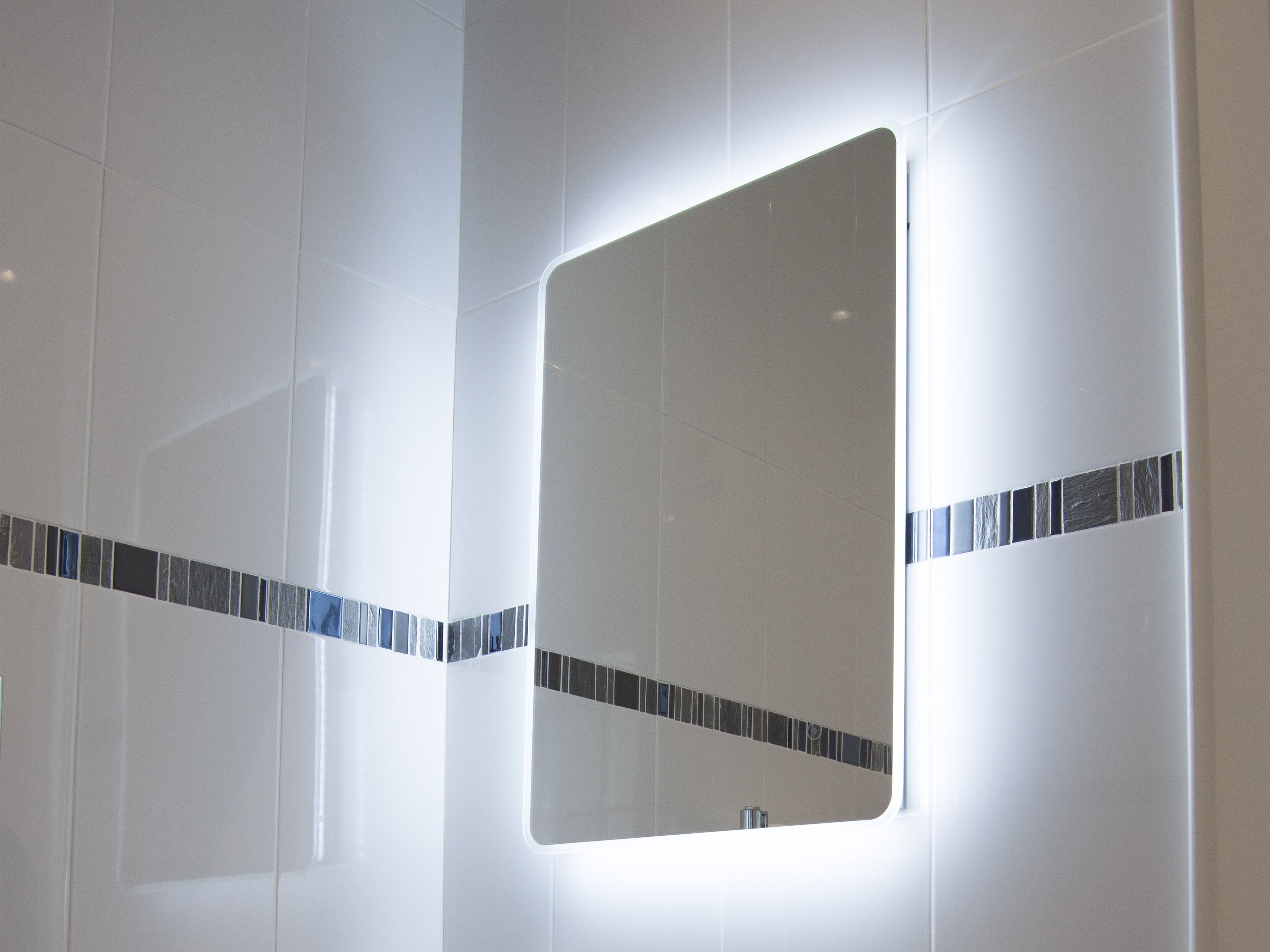 A bathroom with white tiles and a mirror with a light strip.