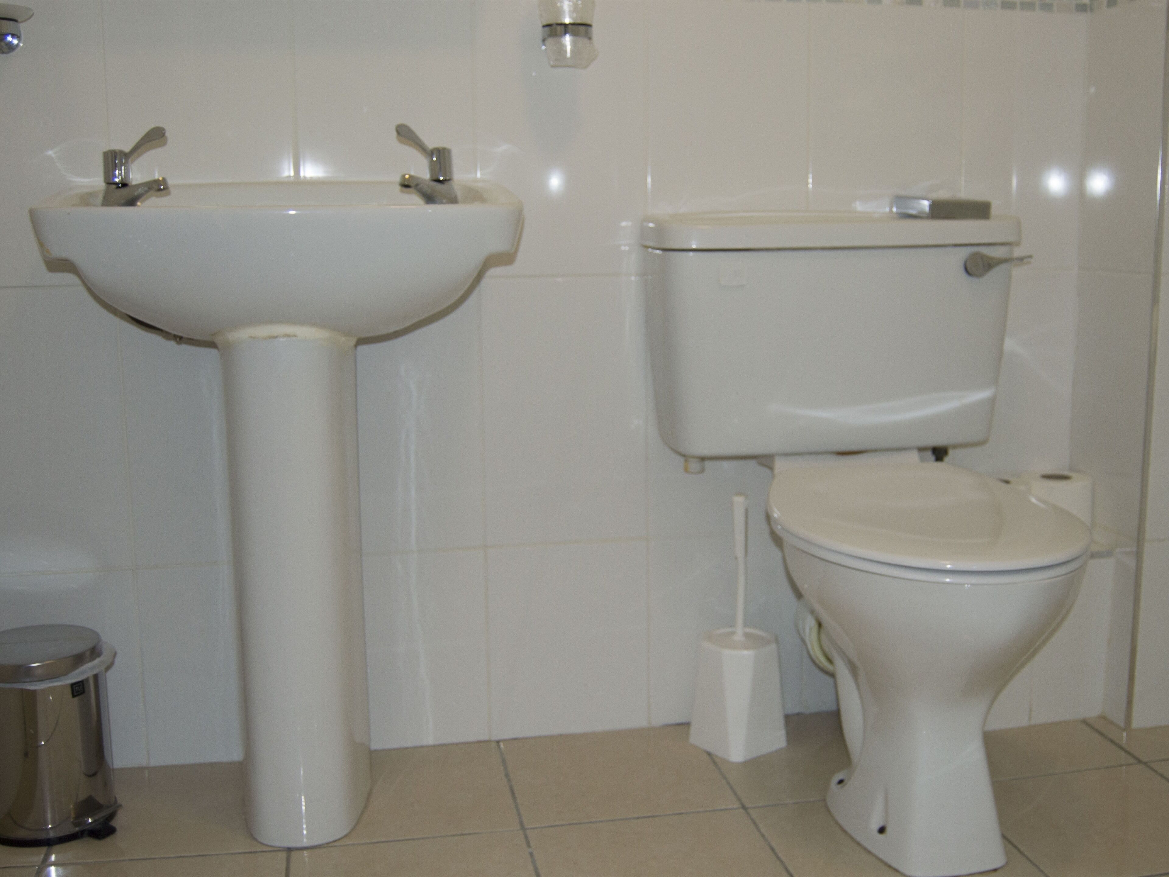 Un baño con lavamanos pedestal, inodoro y cubo de basura.