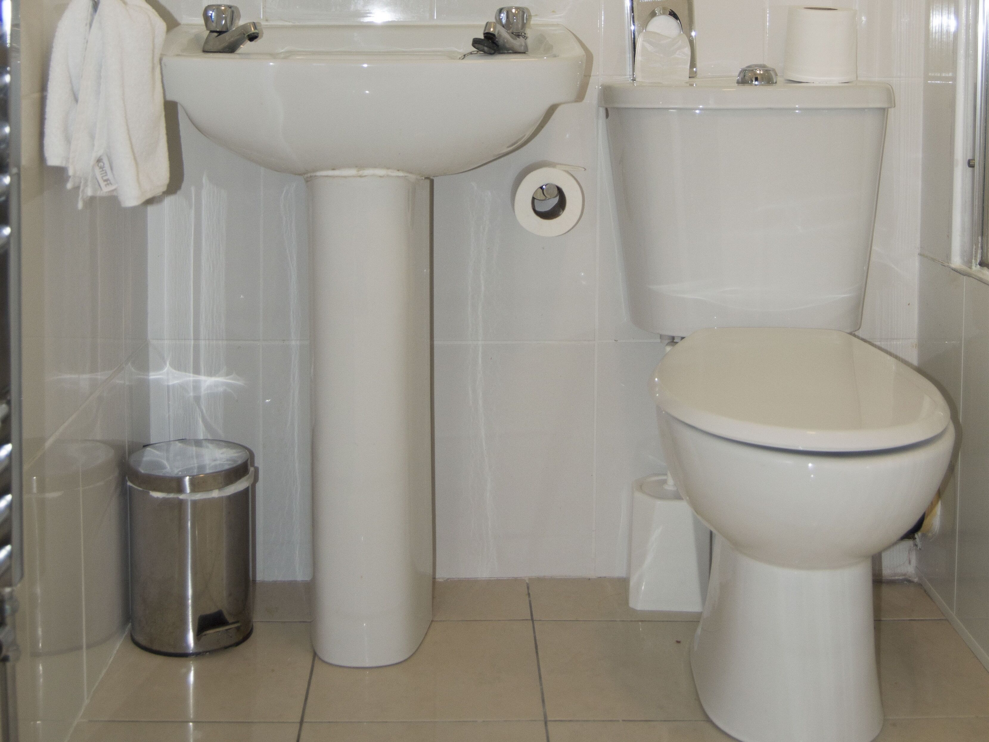 A bathroom with a sink, toilet, and trash can.