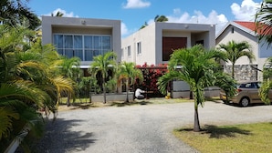 Um edifício moderno com entrada de automóveis em cascalho, palmeiras e um carro estacionado.