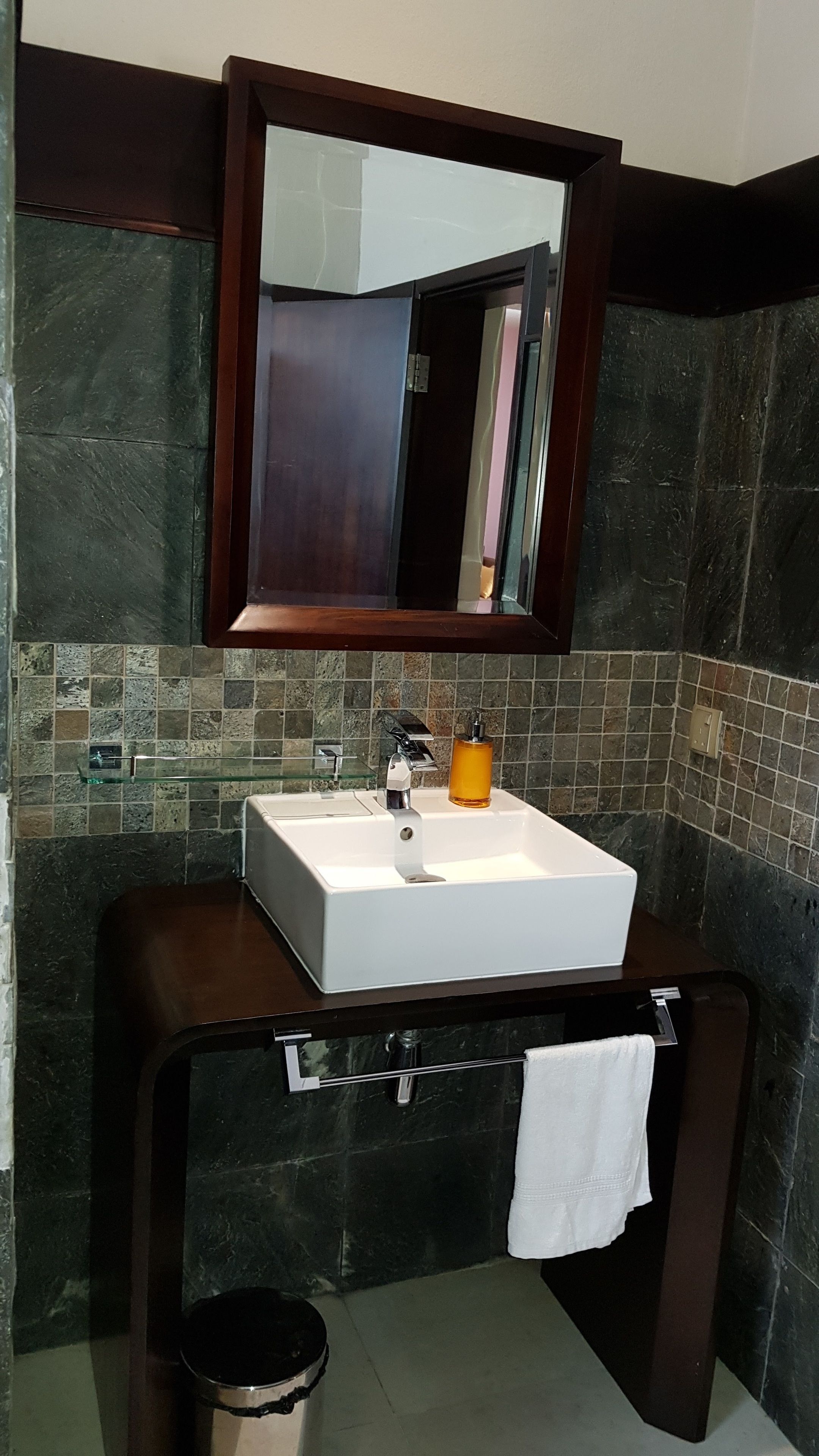 A bathroom with a white sink, a mirror above it, and a dark tiled wall.