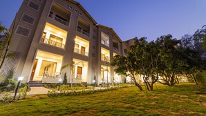 A multi-story hotel with balconies, a well-lit entrance, and a landscaped garden. - La Savanna (Ramnagar)