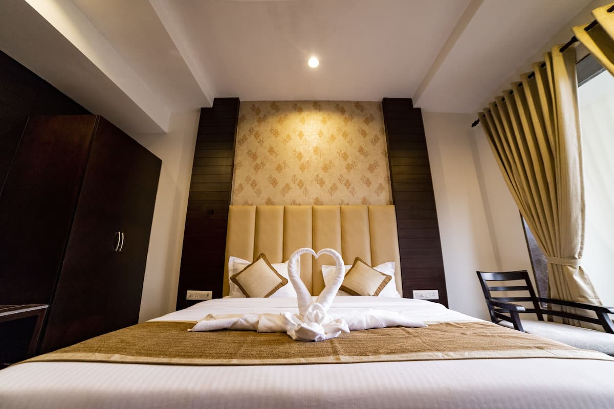 Una habitación de hotel con una cama grande, un cabecero con diseño estampado y un par de toallas con forma de corazón sobre la cama.