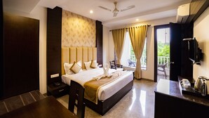 A hotel room with a bed, bedside table, desk, chair, and a balcony with a view. - La Savanna (Ramnagar)