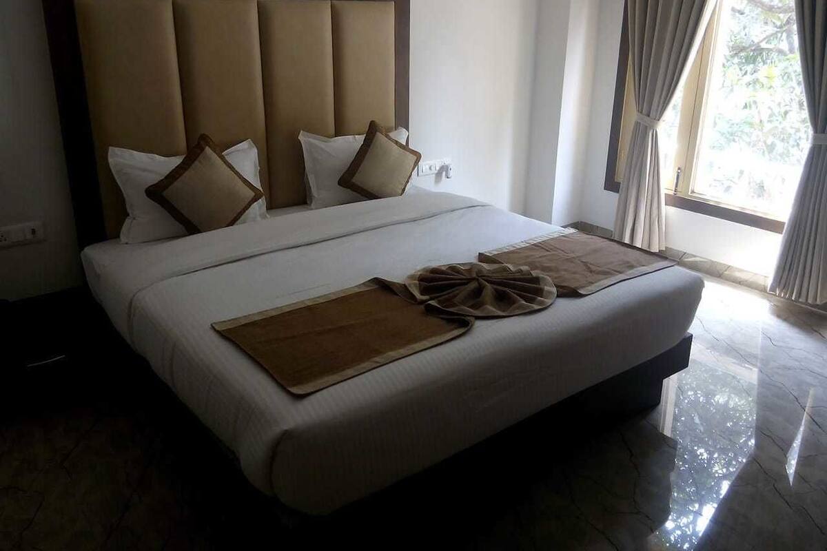 Una cama grande con cabecera acolchada, ropa de cama blanca y dos mantas marrones.