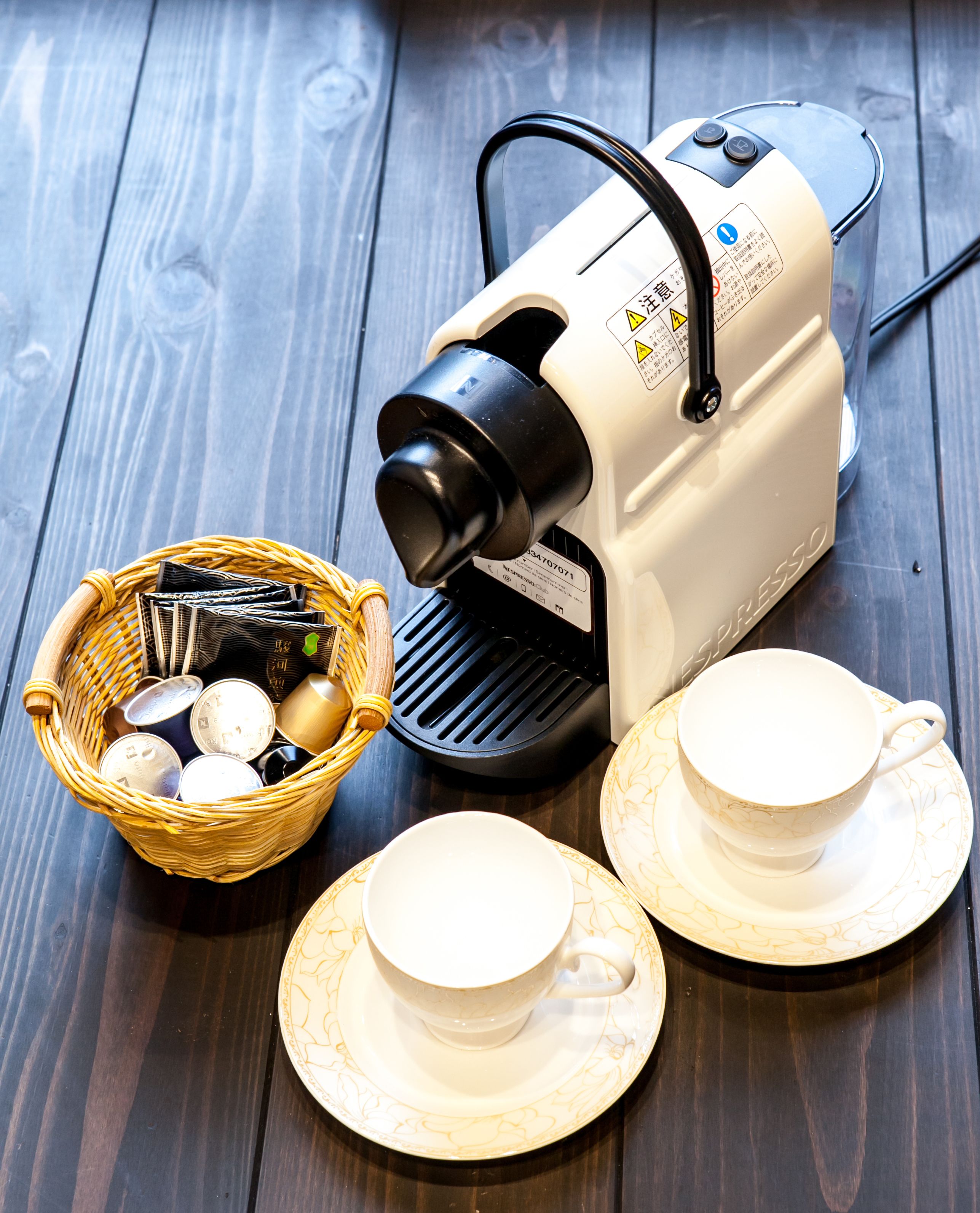 A coffee maker, two cups, and a basket with tea bags on a wooden surface.