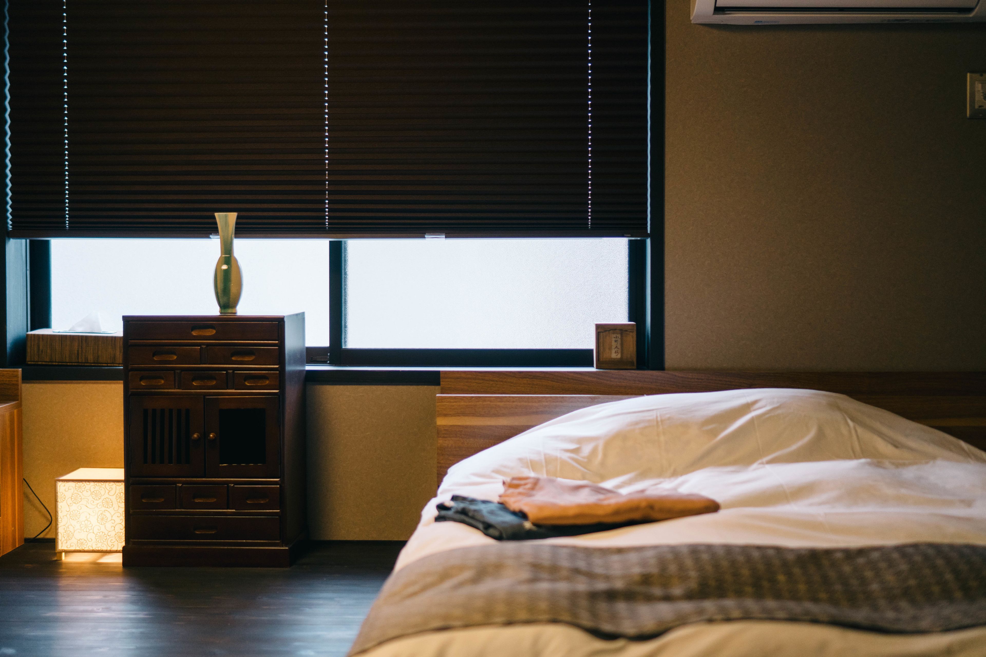 A bedroom with a bed, a dresser, a lamp, and a window with blinds.
