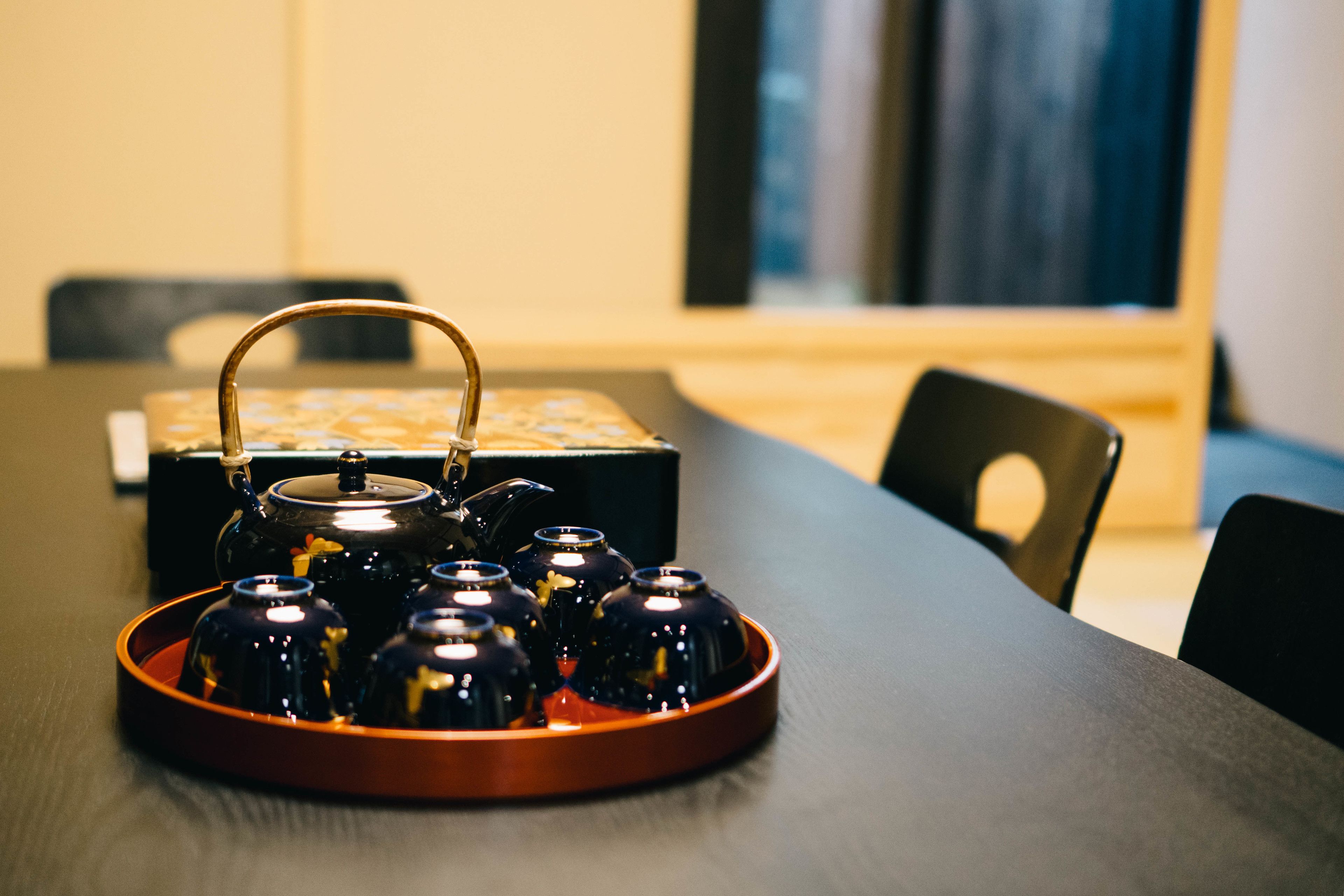 A tray with teapots on a table in a room with a window and chairs.