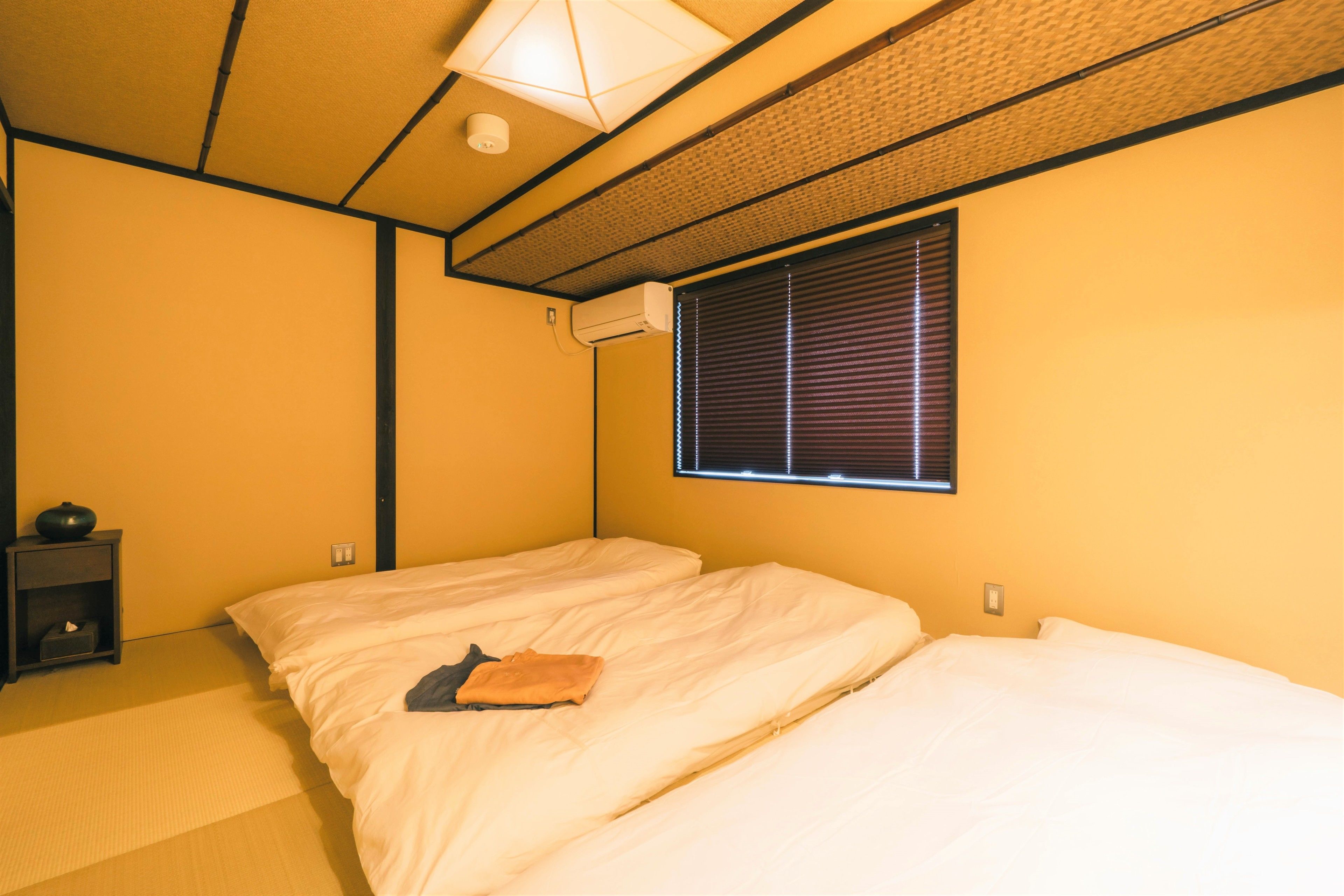 A room with two beds, a small table, and a window with blinds.