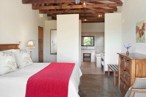 A bedroom with a large bed, a wooden headboard, a red throw blanket, a nightstand with a lamp, and a wooden dresser. - Ama Casa Cottages (Cathkin Park)