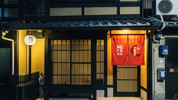 Een traditioneel Japans gebouw met een betegeld dak, een houten poort en een bord met Japanse tekens.