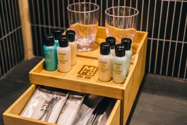A wooden tray with various toiletries including shampoo, conditioner, and body soap, along with two glasses of water.