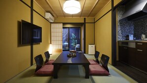 Een traditionele Japanse kamer met tatami vloeren, een lage tafel met kussens, een televisie en een keukenhoek met betegelde spatwand.