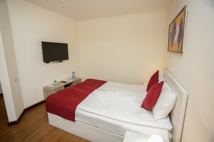 Een hotelkamer met een bed, een flatscreen televisie aan de muur, een nachtkastje met een fles water en een schilderij.