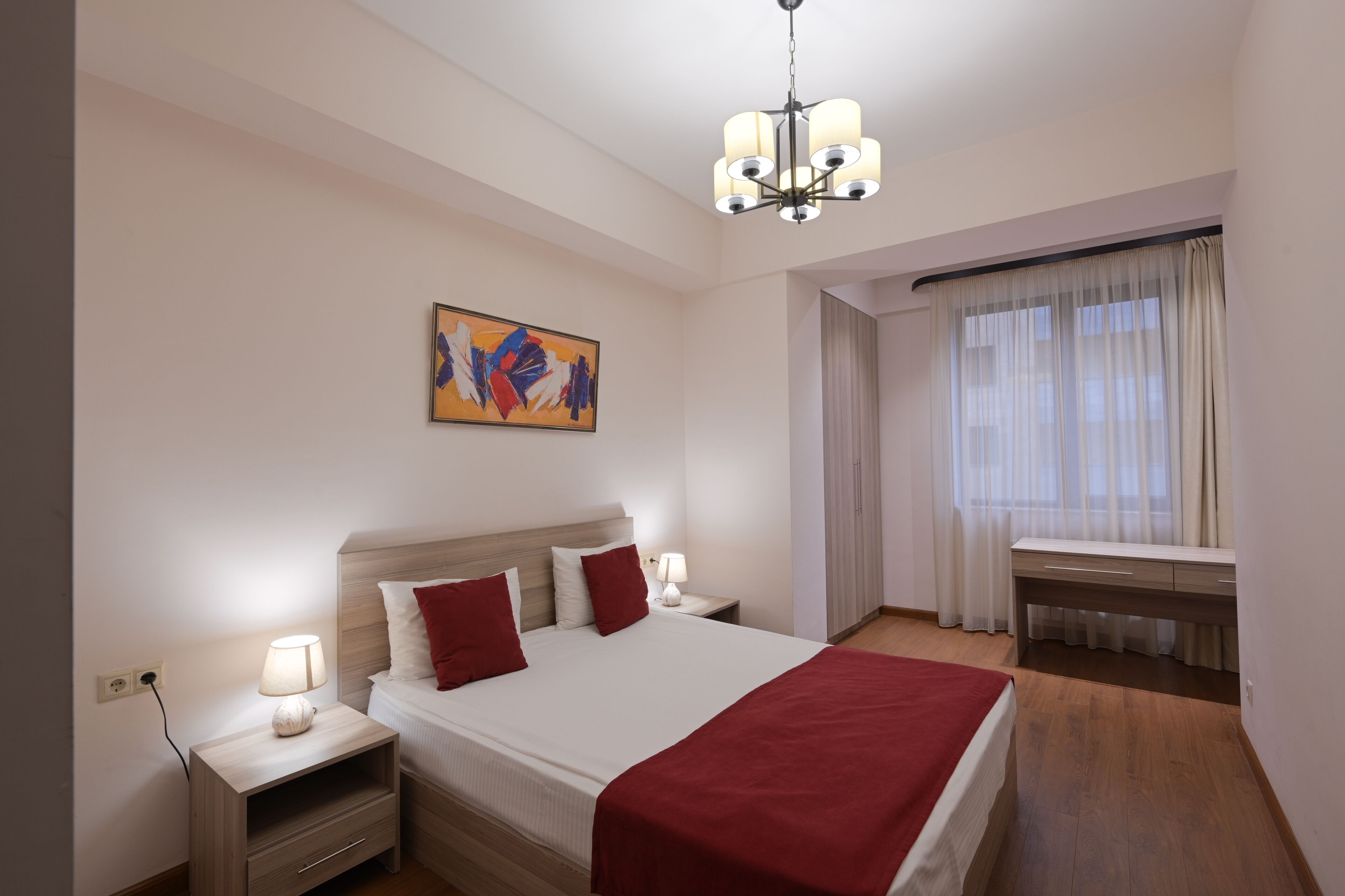 Ein Hotelzimmer mit Bett, Nachttischen, Schreibtisch und einem Fenster mit Vorhängen.