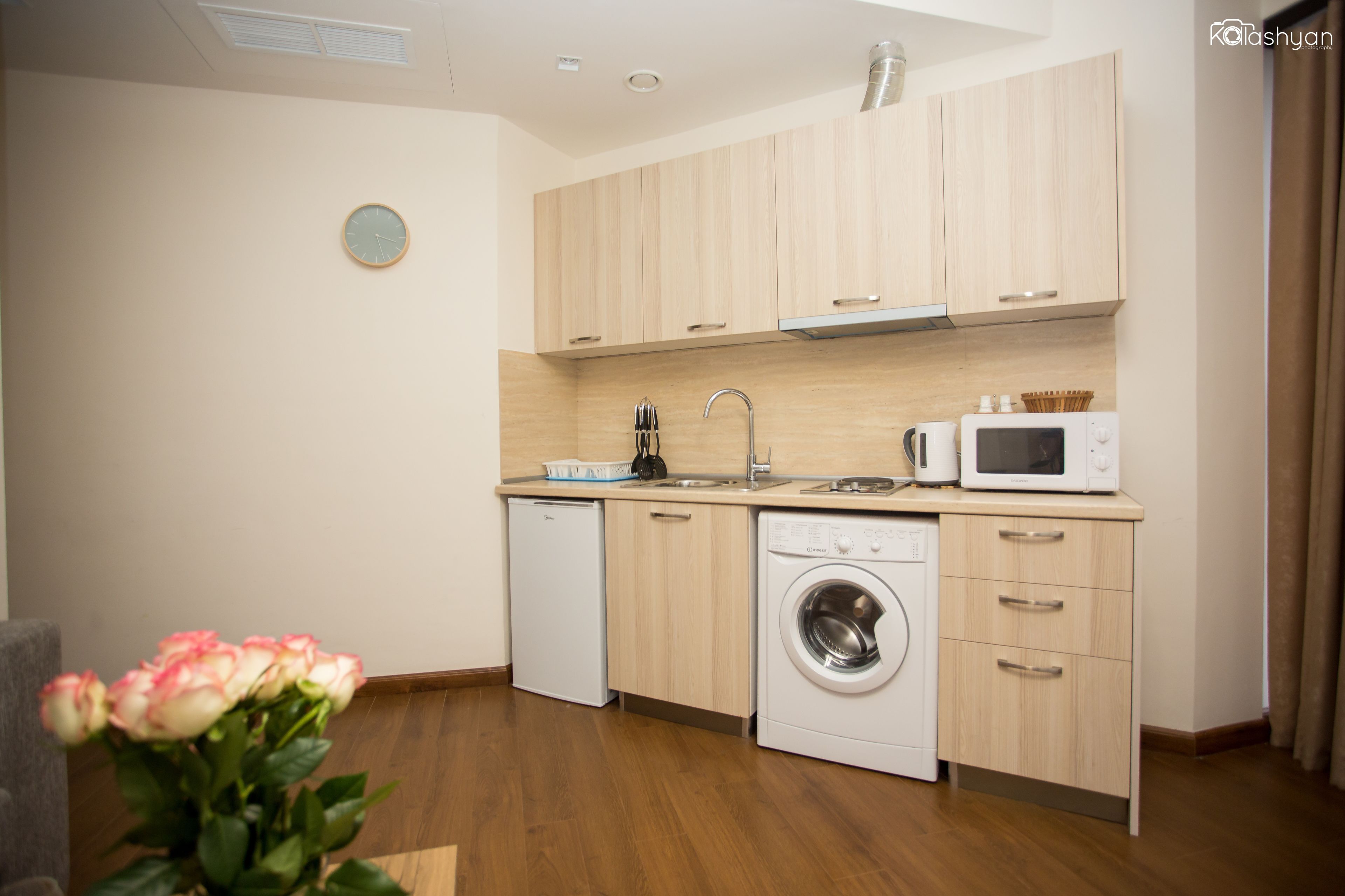 A modern kitchen with wooden cabinets, a dishwasher, a washing machine, and a microwave.
