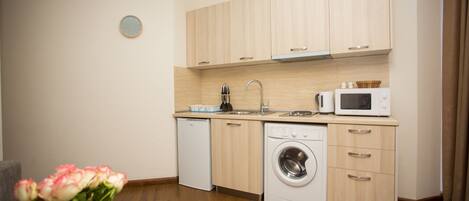 A modern kitchen with wooden cabinets, a dishwasher, a washing machine, and a microwave.