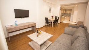 A modern living room with a sofa, a coffee table, a TV, and a dining area with chairs and a table. - Welcome City Center Apartments (Yerevan)