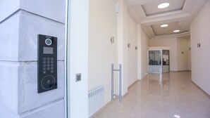 A modern hallway with a wall-mounted elevator control panel, a radiator, and a glass door leading to another room. - Welcome City Center Apartments (Yerevan)
