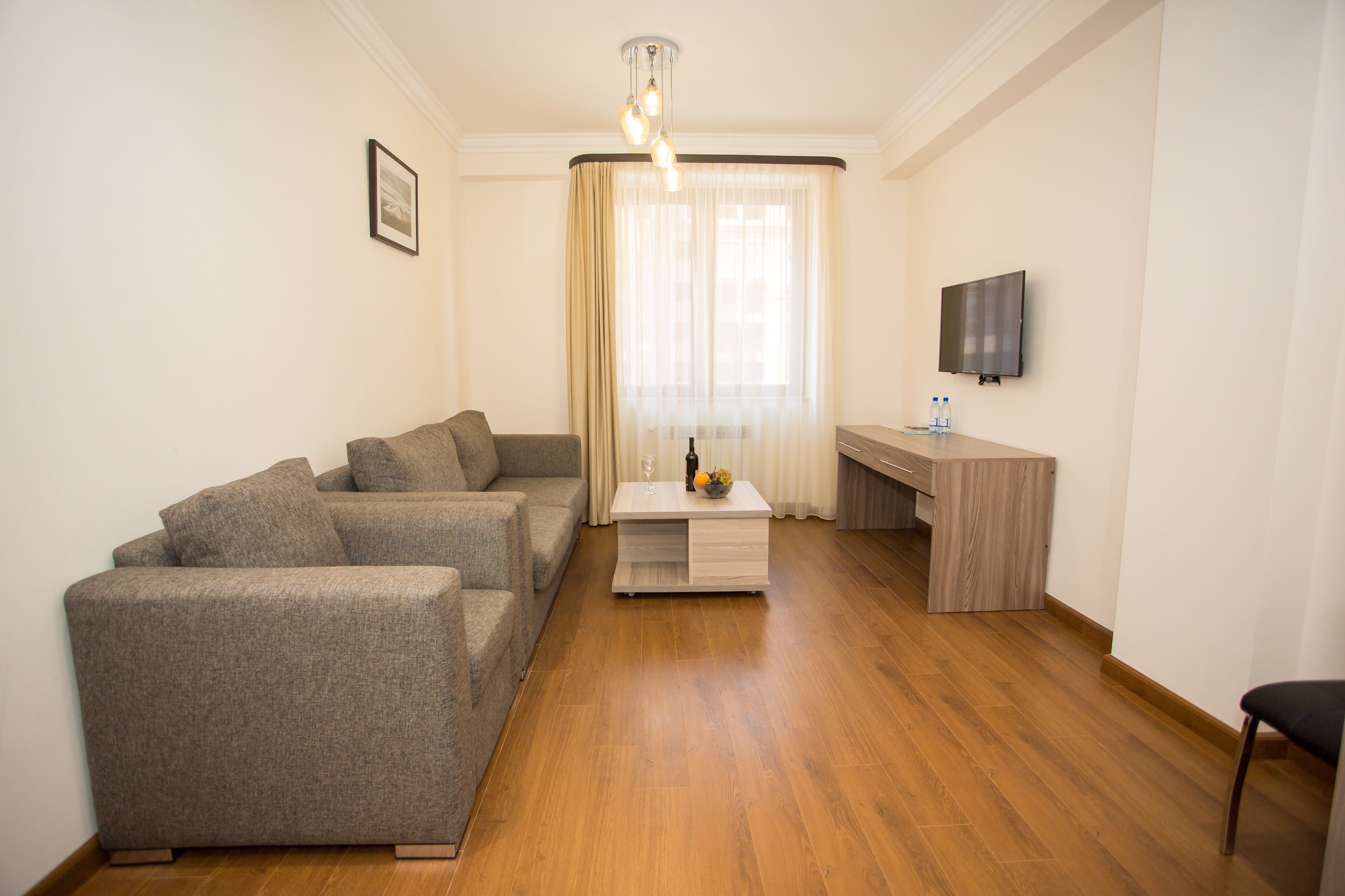 A modern living room with a grey sofa set, a wooden coffee table, and a flat-screen TV mounted on the wall.