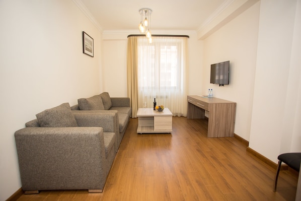 A modern living room with a grey sofa set, a wooden coffee table, and a flat-screen TV mounted on the wall.