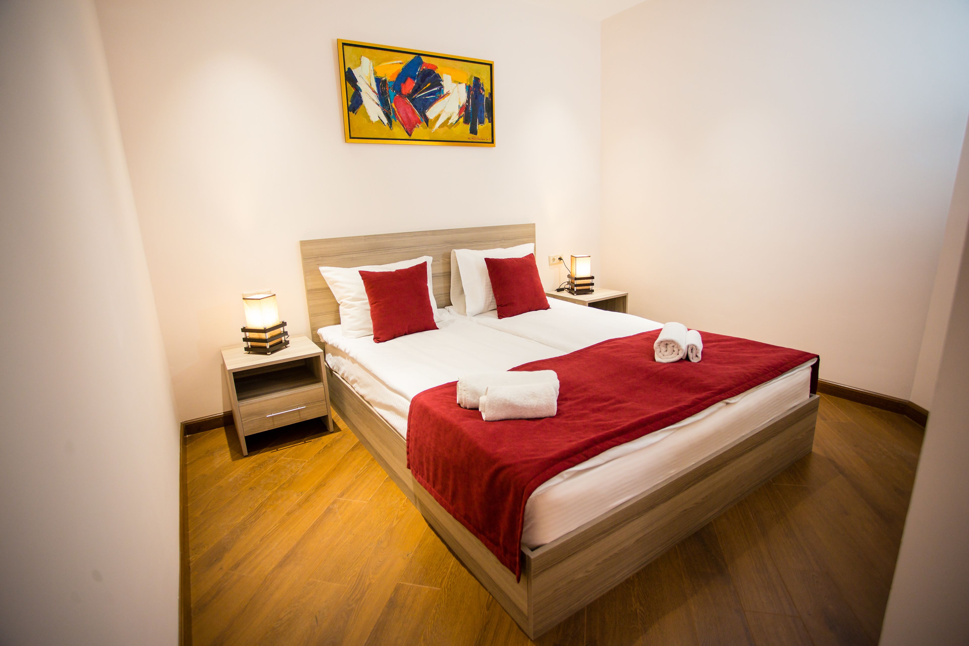 A neatly made bed with white and red bedding, wooden headboard, and two bedside tables with lamps.