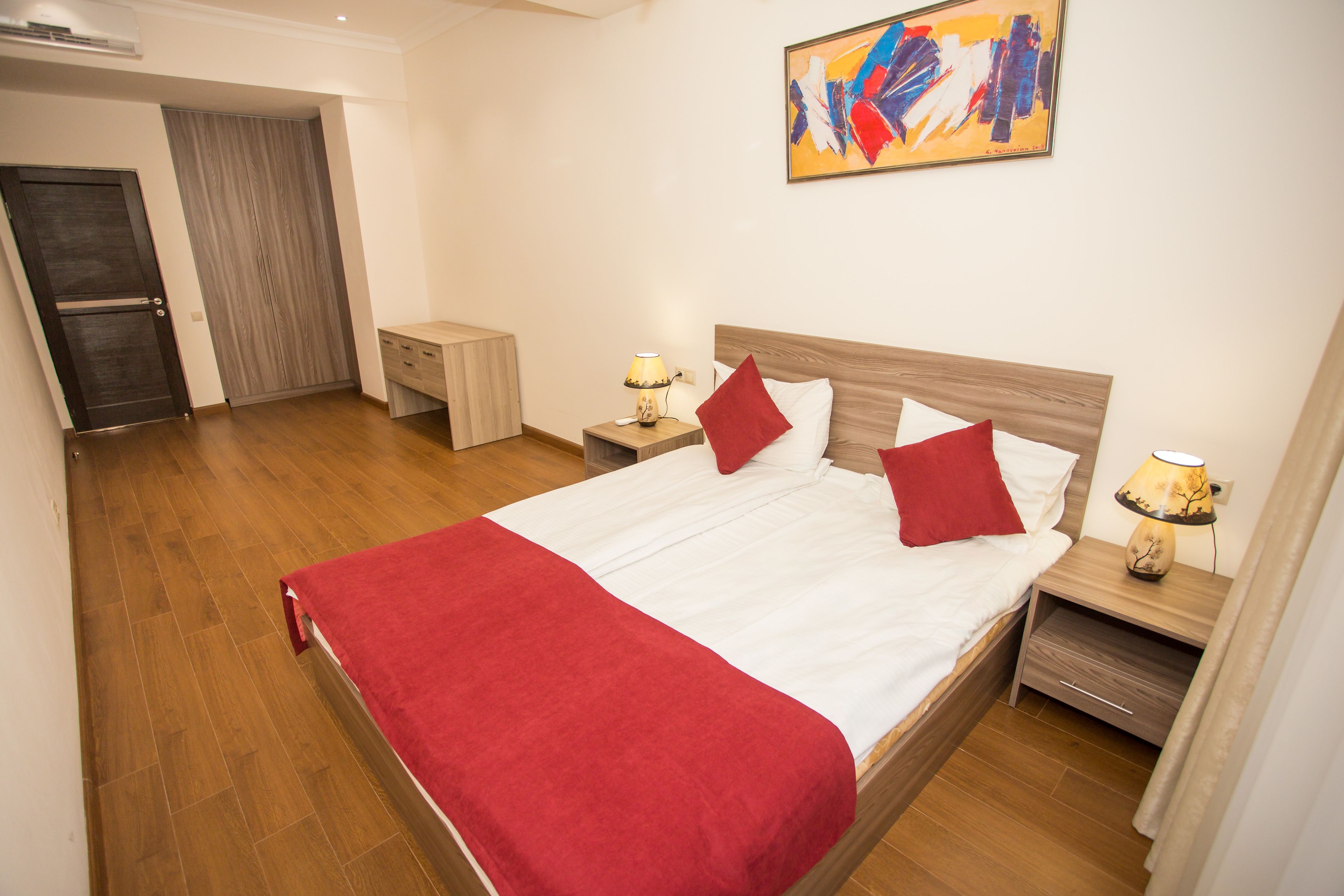 A neatly arranged bedroom with a bed, bedside tables, a nightstand, and a door leading to another room.