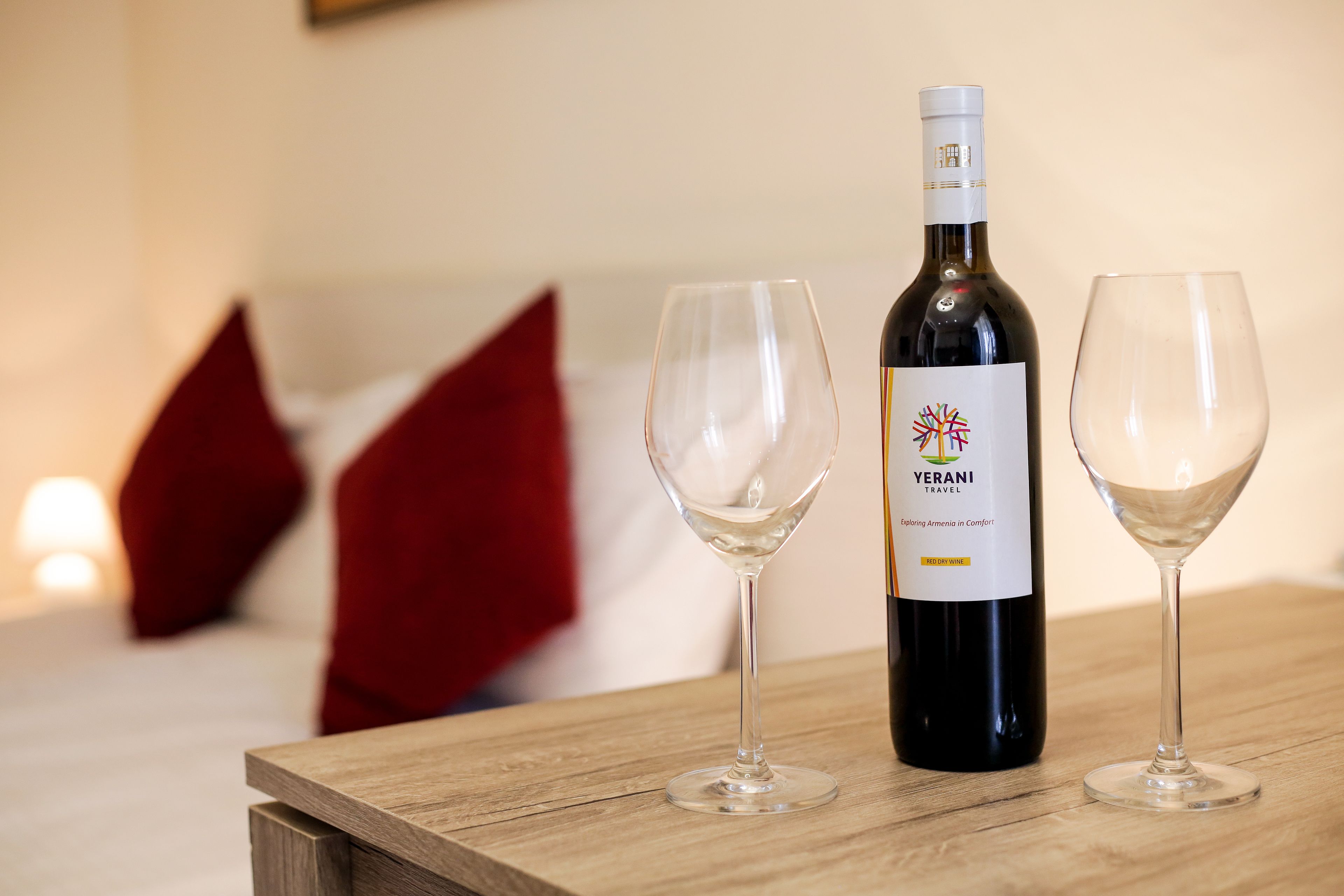 A bottle of wine and two glasses on a wooden table in a hotel room.
