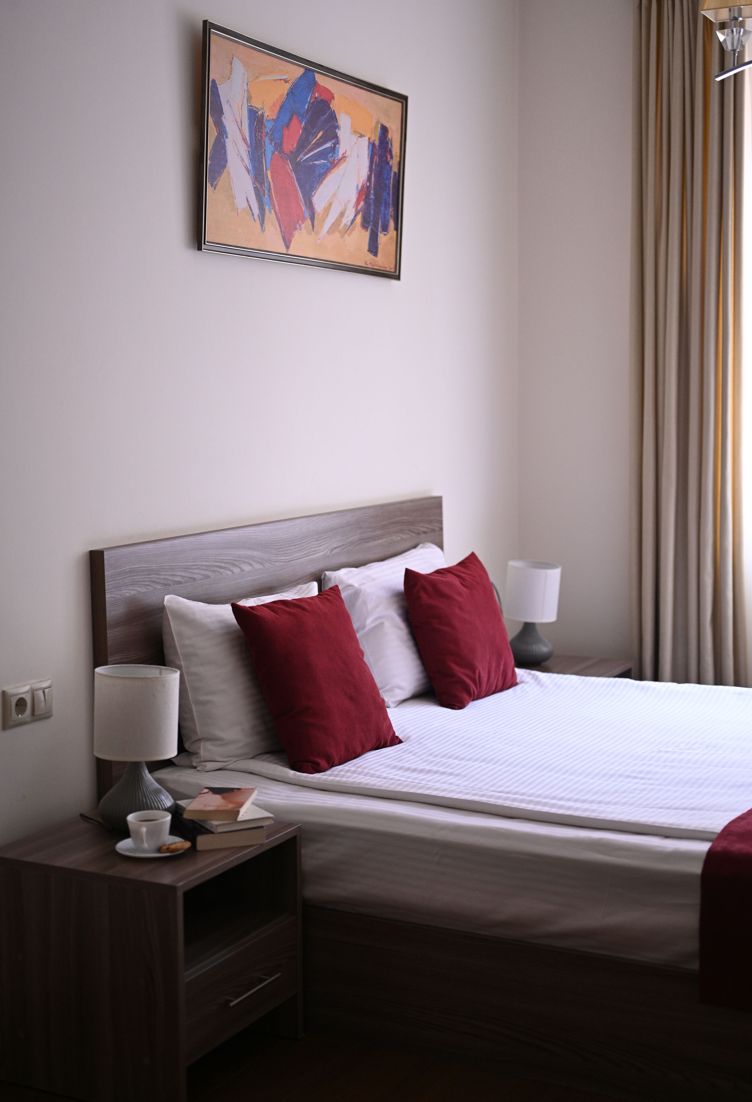 Een hotelkamer met een groot bed, twee nachtkastjes, een lamp, een boek en een beker.