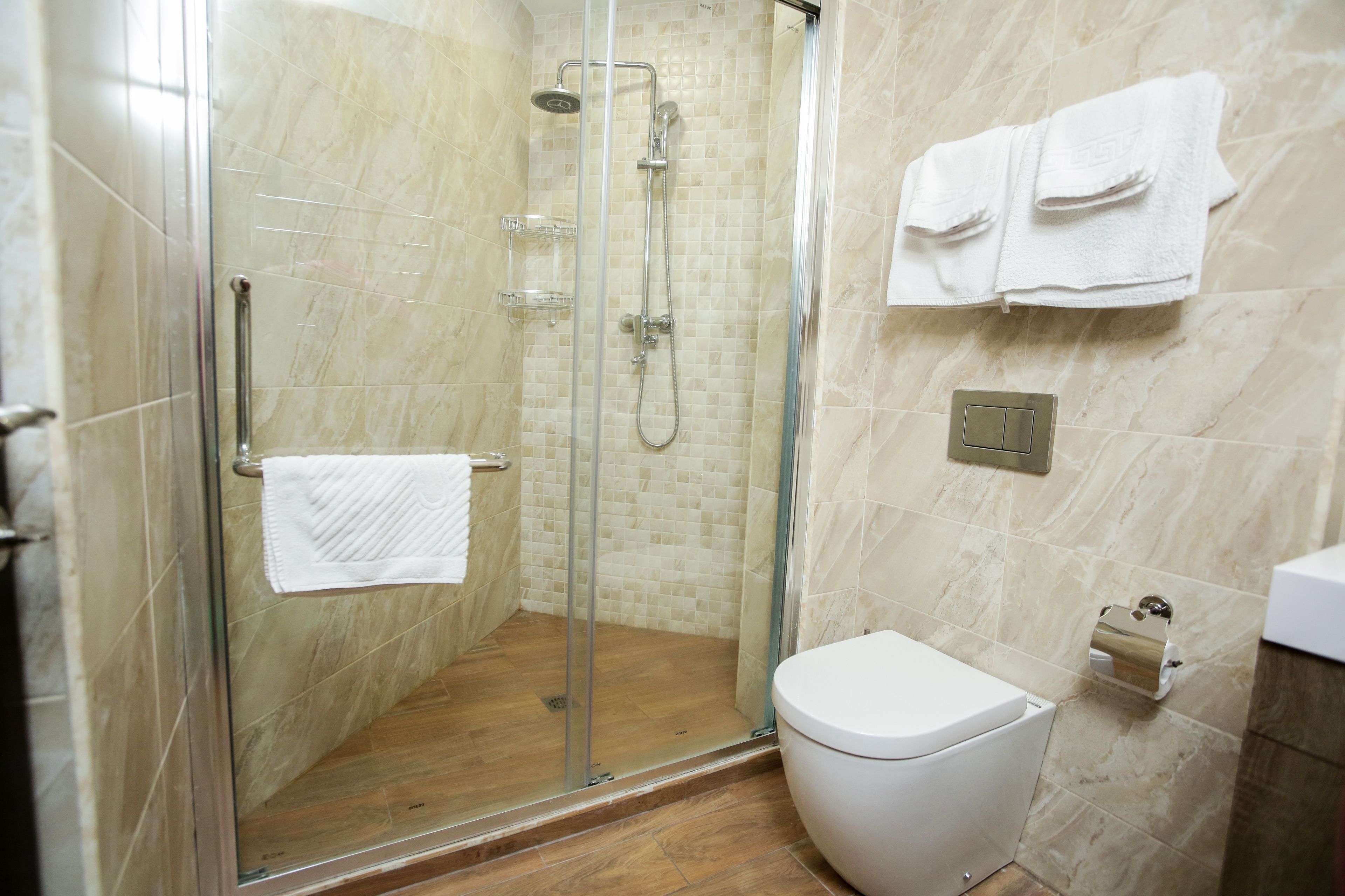 A modern bathroom with a glass-enclosed shower, a white toilet, and a towel rack with folded towels.