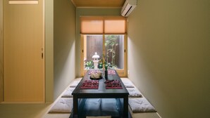 Una habitación japonesa tradicional con suelo de tatami, una mesa baja con un juego de té y vistas a un jardín a través de una puerta corredera.