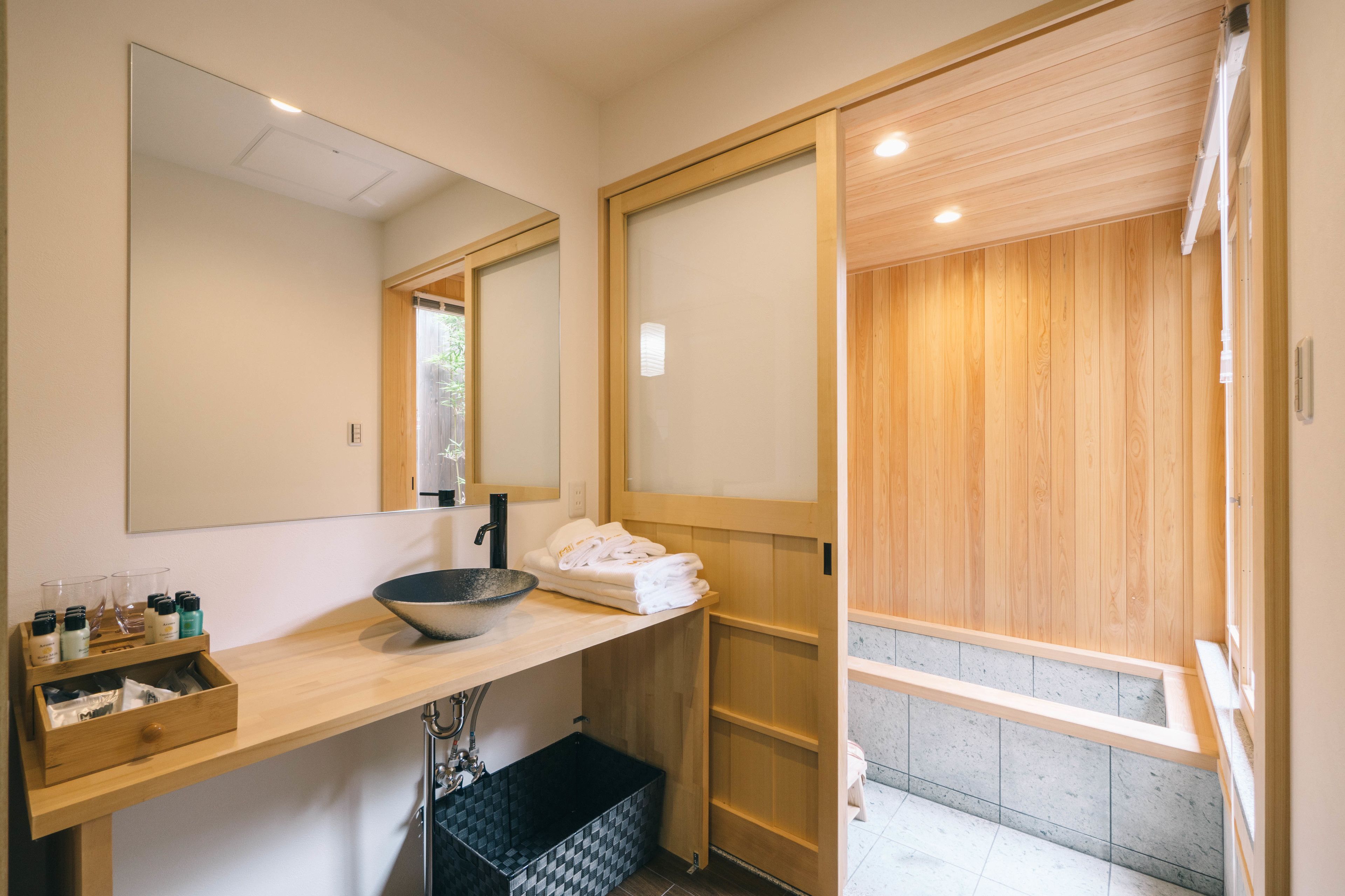 A modern bathroom with a wooden vanity, a large mirror, and a wooden sauna door.
