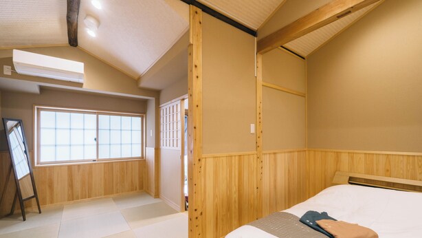 A room with tatami flooring, a bed with a blanket and pillow, a wooden headboard, a window with shoji screens, and a wall-mounted air conditioner. - Miro Saiinnishi Imadacho Tei (Kyoto)