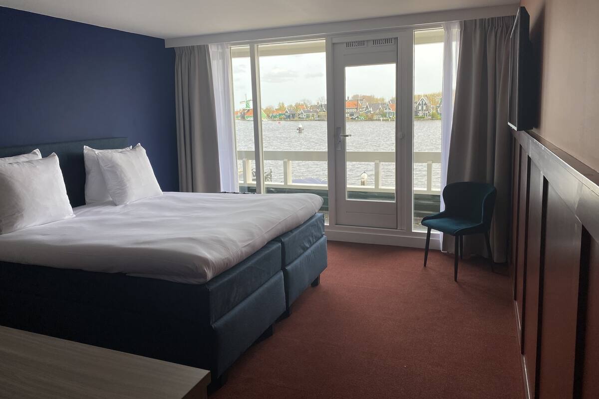 Une chambre d’hôtel avec un grand lit, une chaise et une vue sur une étendue d’eau, accessible par une porte coulissante.