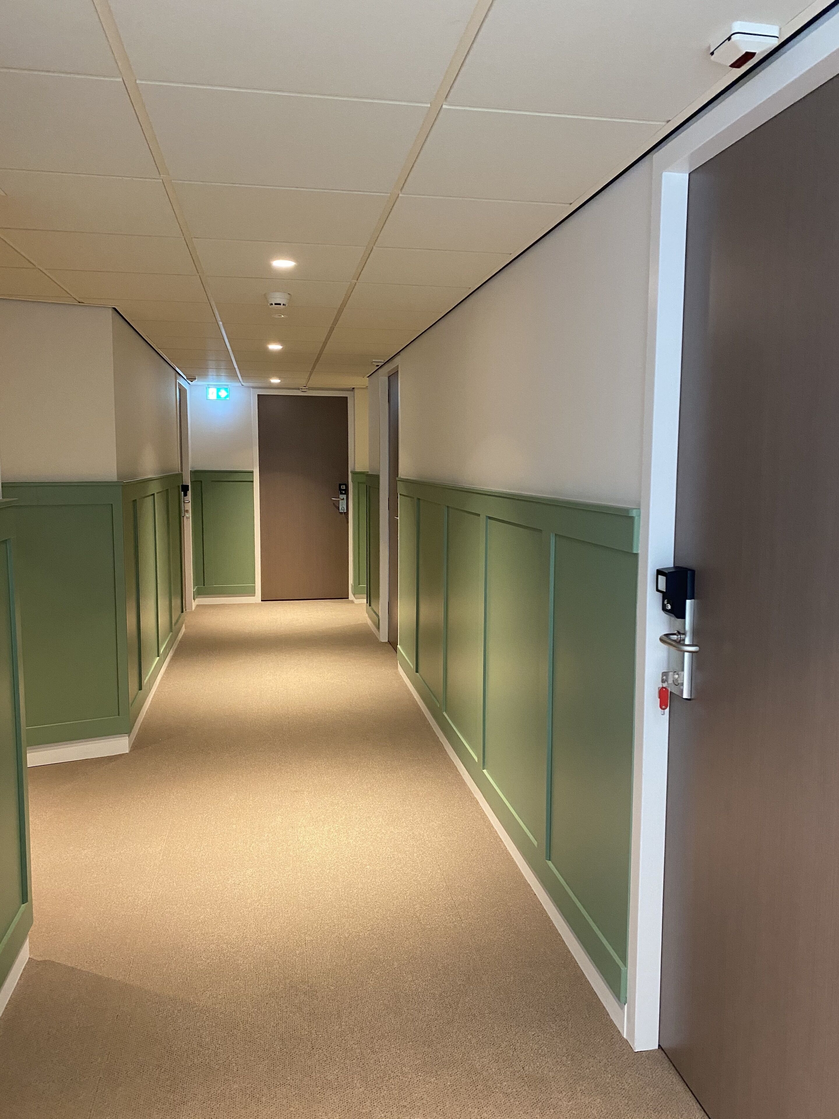 Um corredor com painéis verdes, carpete bege e uma porta com fechadura.