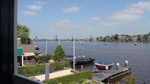 A riverside view with boats docked, a windmill, and houses along the water. - Boutique Hotel Zaan (Zaandijk)