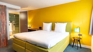 A hotel room with a large bed, a bedside table, a lamp, and a bathroom visible through an open door.