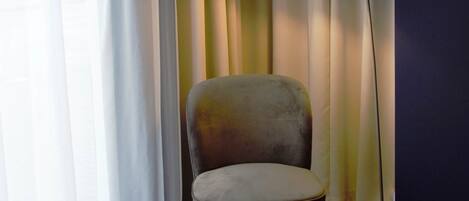 A corner room with a chair, a floor lamp, and curtains.