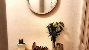 Une console en bois, ornée d’un miroir, d’une plante en pot et d’une décoration représentant le mot « amour ».