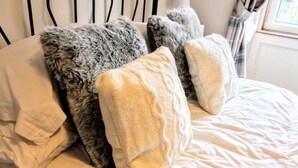 Un lit avec une couette blanche et plusieurs oreillers, dont un oreiller gris moelleux et un oreiller beige tricoté.