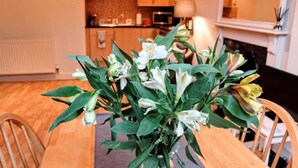 Une table à manger agrémentée d’un centre de table floral, des chaises en bois et une cuisine en arrière-plan.