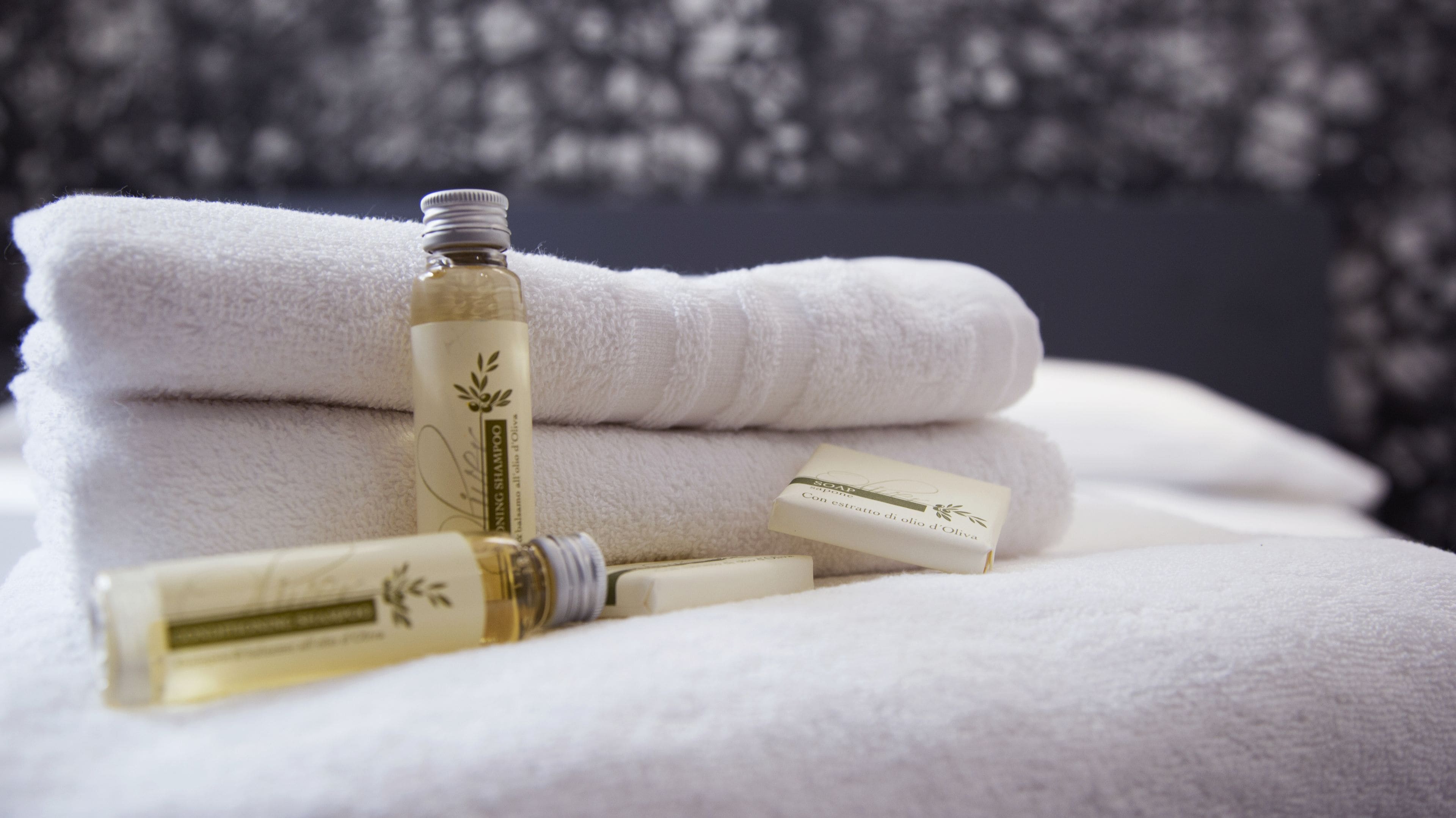 A stack of white towels and a bottle of olive oil soap on a white surface.